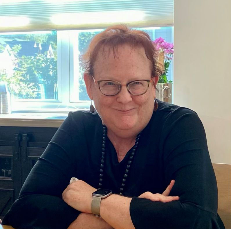 Linda Tate, a woman with short hair and glasses is grinning